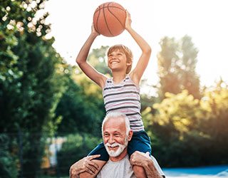 a grandparent with their grandchild on their shoulders playing basketball