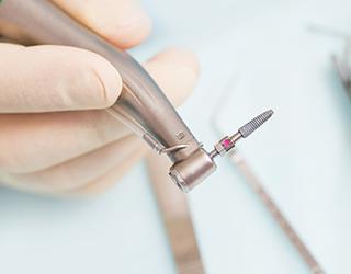 A dental instrument holding a titanium implant post in Coral Springs