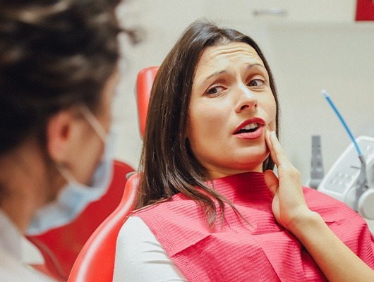 woman holding cheek speaking with dentist