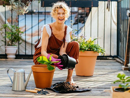 person kneeling on a patio and placing new plants in planters
