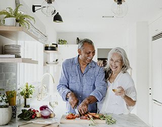 a couple chopping vegetables for dinner while drinking wine in the kitchen