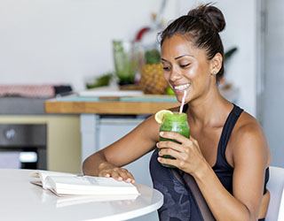 a person sitting down at a table, reading a book, and drinking a homemade healthy smoothie