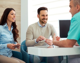 Couple discussing cost of dental implants with dentist