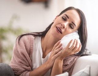 Woman sitting on couch and holding cold pack against cheek