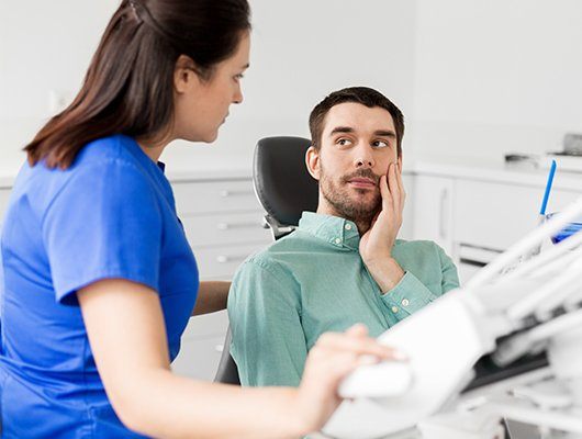 man holding cheek in exam chair looking at team member