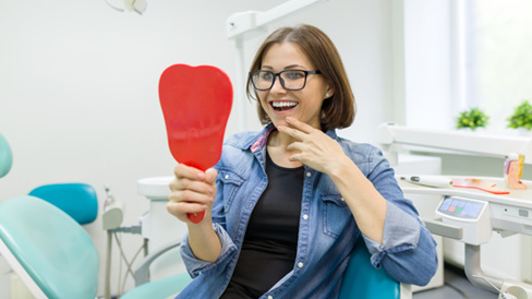 Middle-aged woman smiling in the mirror at dentist’s office 