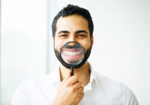 young man using magnifying glass to showcase his dental implants in Coral Springs 