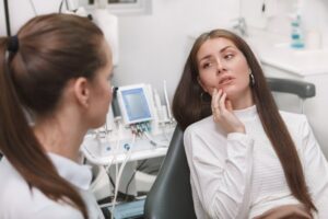 Woman in dentist's chair holding mouth in pain.