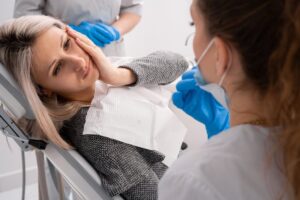 Woman holding her jaw in pain sitting in the dentist's chair.