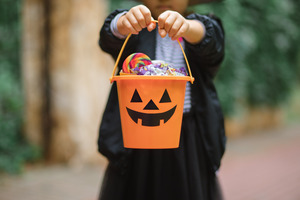 Little girl in witch costume holding out Halloween bucket